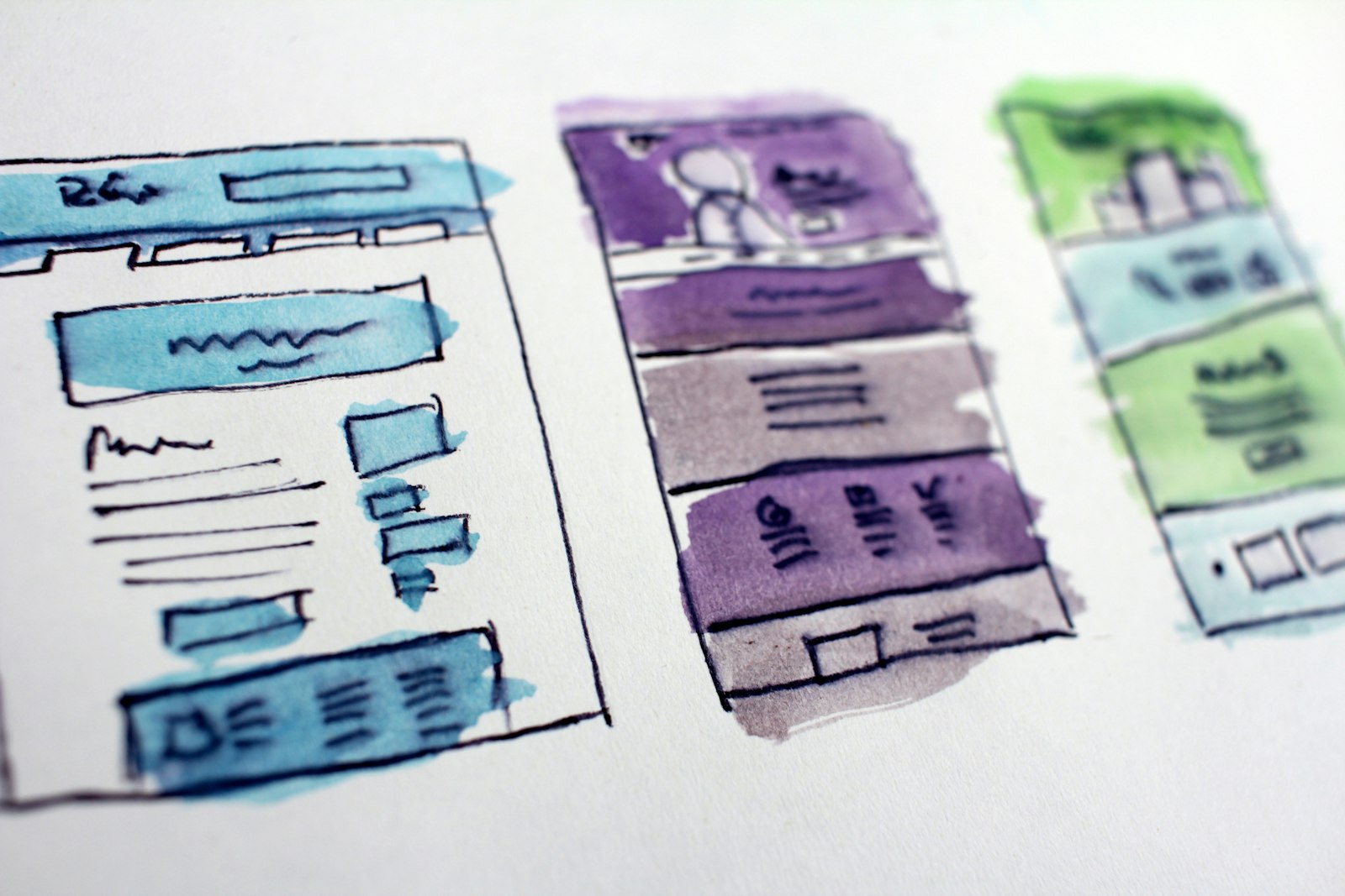 Watercolor wireframe sketches of website page layouts on paper, showing desktop and mobile arrangements.
